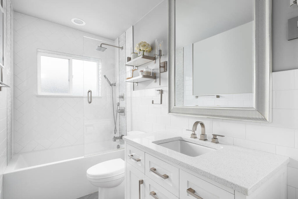 A bathroom with a white vanity cabinet, granite countertop, and a shower lined with large herringbone tiles. - Фото, изображение