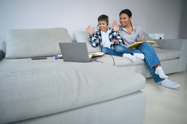 Online learning at home, a boy and his mom are sitting on the couch with a laptop, headset, books - Φωτογραφία, εικόνα