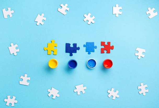 World Autism Awareness Day or month concept. Creative design for April 2. White puzzles, symbol of awareness for autism spectrum disorder and colorful paints on blue background. Top view, copy space. - Fotografie, Obrázek
