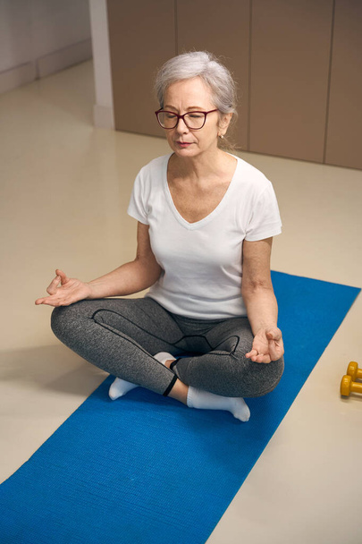 Yoga training for the elderly, a woman meditates in the lotus position, dumbbells lie nearby - Foto, Imagem