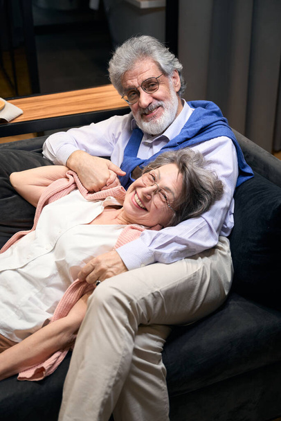 Elderly male and woman resting on sofa in hotel, talking and looking at the camera - Foto, immagini