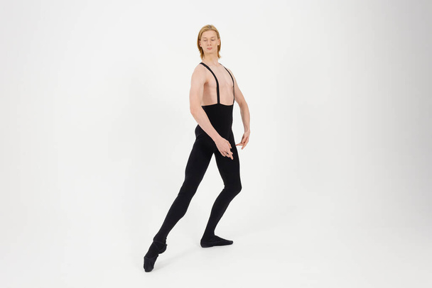 Young Athletic professional ballet dancer with a bare torso and black dance tights in a perfect shape performing over the white background. - Foto, Imagem