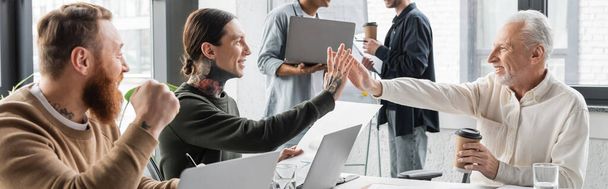 Positieve zakelijke mensen geven high five in de buurt van collega 's tijdens de opleiding in het kantoor, banner  - Foto, afbeelding