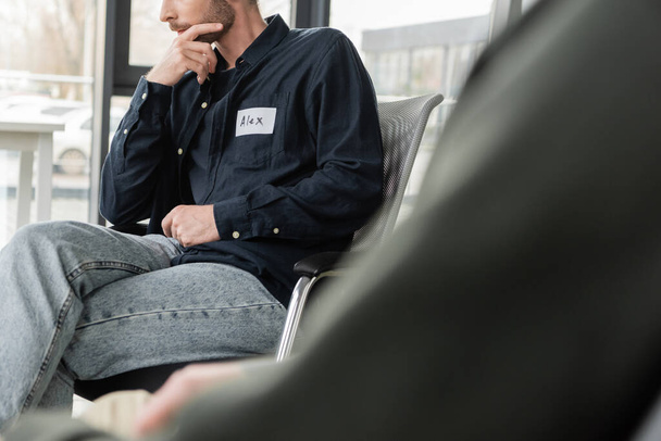 Обрезанный вид человека с алкогольной зависимостью, сидящего на стуле в реабилитационном центре  - Фото, изображение