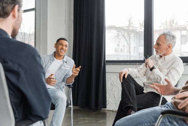 Homem americano africano alegre com dependência de álcool conversando durante sessão de terapia de grupo no centro de reabilitação  - Foto, Imagem