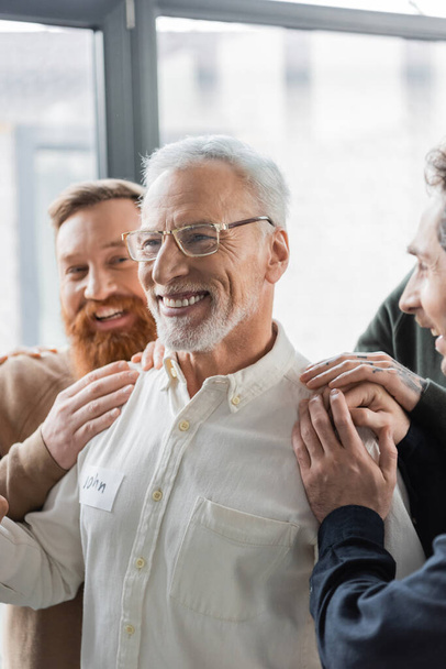 Persone positive che abbracciano l'uomo di mezza età con dipendenza da alcol durante la terapia di gruppo nel centro di riabilitazione  - Foto, immagini