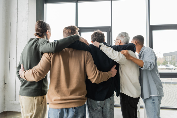 Rückansicht multiethnischer Menschen mit Alkoholabhängigkeit, die sich während der Therapie im Reha-Zentrum umarmen  - Foto, Bild