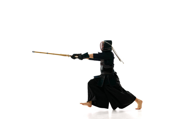 Strength. Man, professional kendo athlete in black uniform with sword, shinai training against white studio background. Concept of martial arts, sport, Japanese culture, action and motion - Foto, Bild