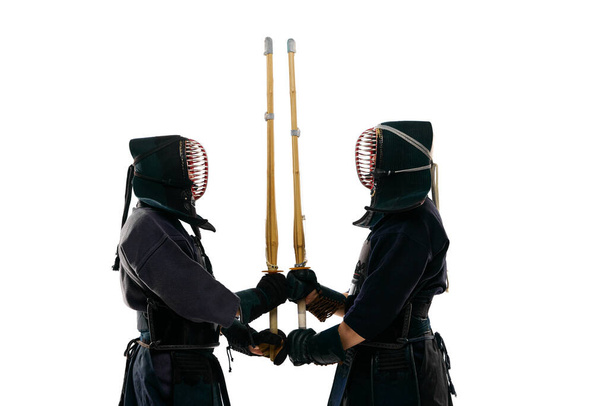 Sword to sword. Two men, professional kendo fighter, athletes in black uniform training against white studio background. Concept of martial arts, sport, Japanese culture, action and motion - Fotó, kép