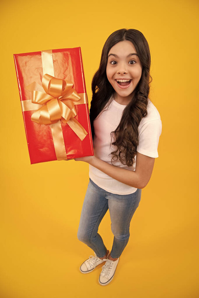 Amazed teenager. Child with gift present box on isolated studio background. Gifting for kids birthday. Excited teen girl - Fotó, kép