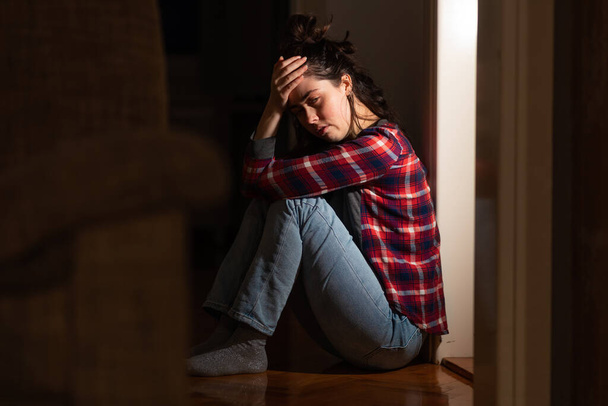 Depressione e disturbi mentali. Sofferente giovane donna caucasica si siede sul pavimento nella disperazione in soggiorno. Concetto di problemi psicologici. - Foto, immagini