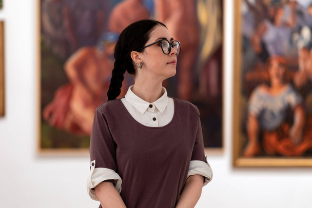 Cultural education. Portrait of caucasian pretty young woman wearing glasses visiting excursion in museum, contemplates arts. Concept of exhibition in gallery. - Fotoğraf, Görsel