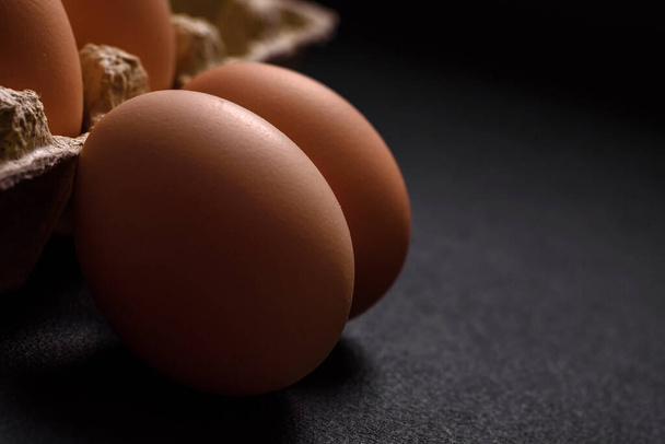 Fresh raw chicken eggs in beige color in a cardboard tray on a dark concrete background - Photo, Image