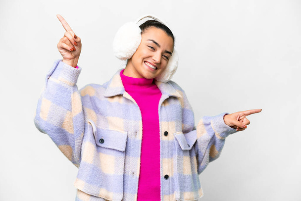 Mujer joven con manguitos de invierno sobre fondo blanco aislado señalando el dedo a los laterales y feliz - Foto, Imagen