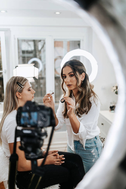 Happy young woman streaming a beauty makeup vlog from home or workshop. Beautiful online content creator cosmetician applying makeup and explaining some work tools. Vlogging and online channel work.  - Foto, afbeelding