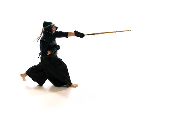 Man, professional kendo athlete in uniform with helmet training with bamboo shinai sword against white studio background. Concept of martial arts, sport, Japanese culture, action and motion - Фото, зображення