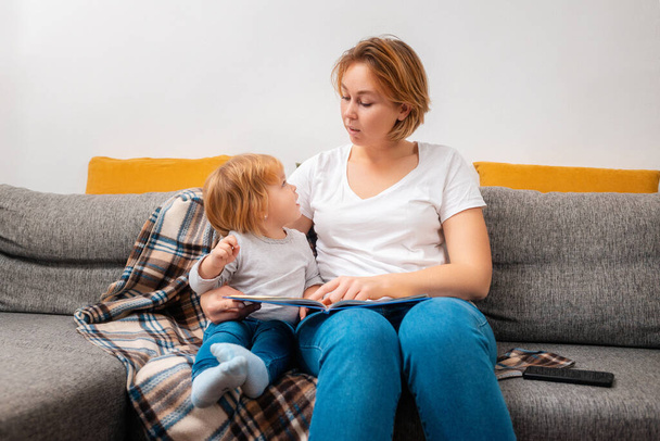 Speech therapist is reading a book to little child sitting on the sofa. Statement of speech pronunciation. The concept of home preschool education. - Foto, afbeelding
