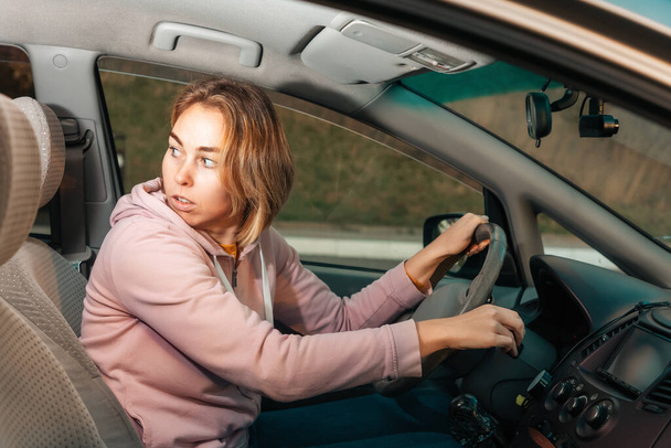 Muotokuva pelokkaasta valkoihoisesta naisesta, joka ajaa vasenkätisellä autolla, katsoo taakse. Sivunäkymä Liikenneonnettomuuksien käsitteet. - Valokuva, kuva