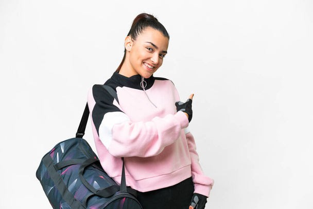 Young sport woman with sport bag over isolated white background pointing back - 写真・画像
