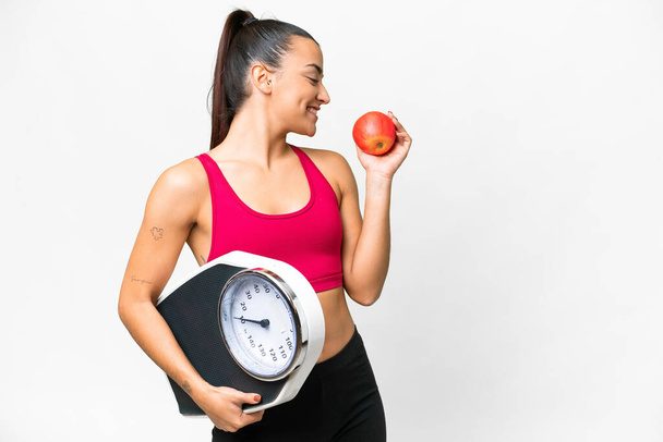 Young beauty woman over isolated white background with weighing machine and with an apple - Valokuva, kuva