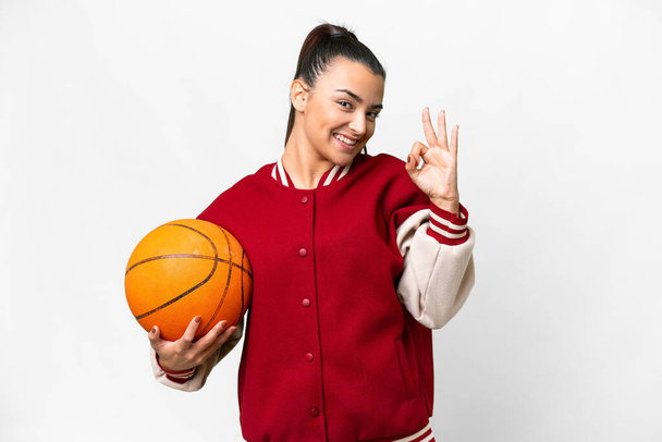 fiatal nő kosárlabda felett elszigetelt fehér háttér mutatja rendben jel ujjakkal - Fotó, kép