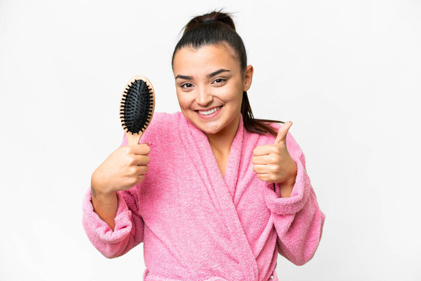 Young woman in a bathrobe with hair comb over isolated white background with thumbs up because something good has happened - Photo, Image