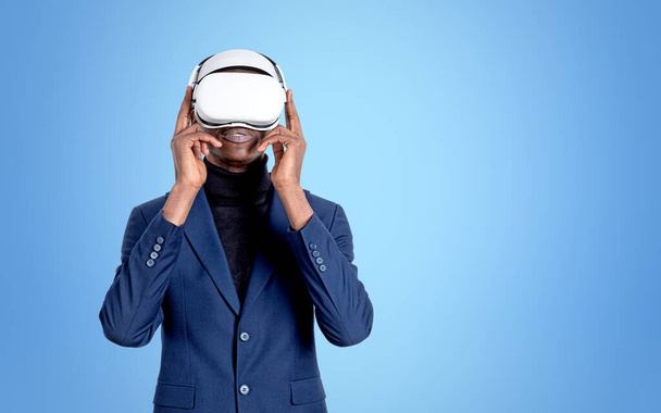 African businessman working in vr glasses headset, standing on light blue background. Concept of metaverse and information fields. Copy space - Фото, зображення