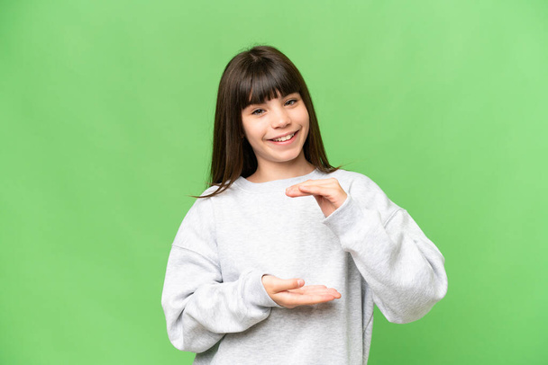 Bambina sopra isolato sfondo chiave croma verde tenendo copyspace immaginario sul palmo della mano per inserire un annuncio - Foto, immagini