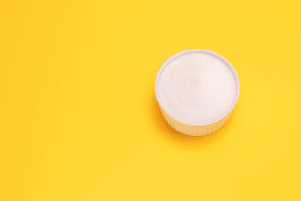 Natural organic sweetener Erythritol, produced by fermentation from corn, called dextrose in ceramic bowl on yellow orange background. Sugar substitute. Horizontal plane, copy space for text. Top view - 写真・画像