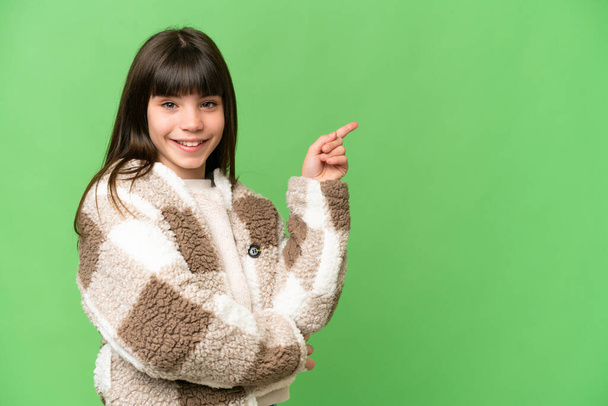 Little girl over isolated green chroma key background pointing finger to the side - Foto, afbeelding