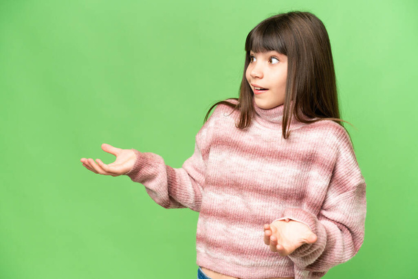 Little girl over isolated green chroma key background with surprise expression while looking side - Foto, Bild