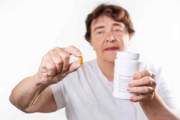 Portrait of an senior smiling woman holding a jar of vitamins. Grandmother looks at the pill. White background. The concept of skin care and health. - Foto, Imagen