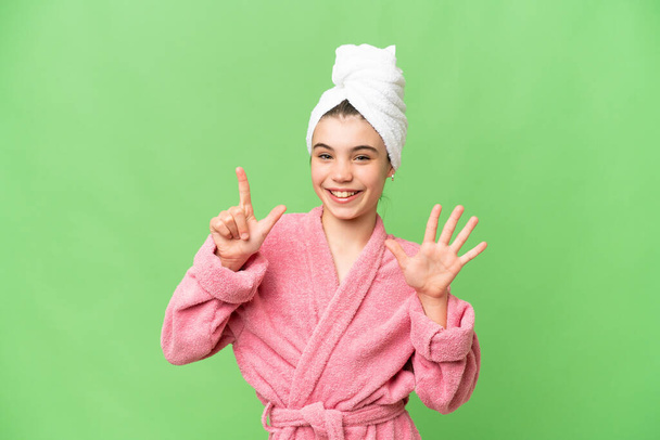 Kleines Mädchen im Bademantel über isoliertem Chroma-Schlüsselhintergrund, der mit den Fingern sieben zählt - Foto, Bild