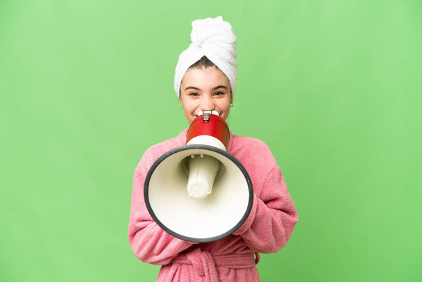 Little girl in a bathrobe over isolated chroma key background shouting through a megaphone - Photo, Image