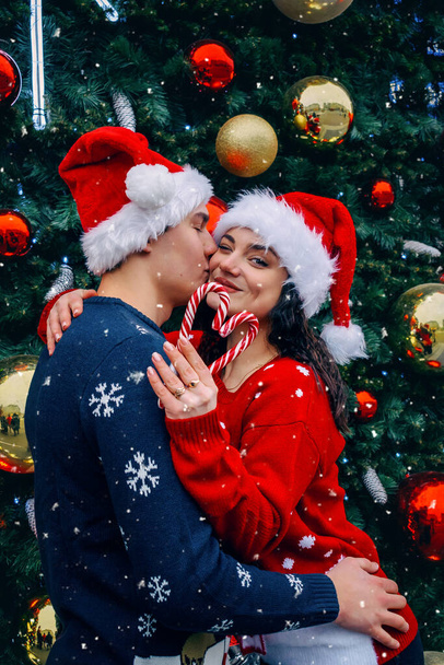 Χριστουγεννιάτικη αγάπη. Άντρας και γυναίκα με καπέλα Σάντα κοντά στο χριστουγεννιάτικο δέντρο.  - Φωτογραφία, εικόνα