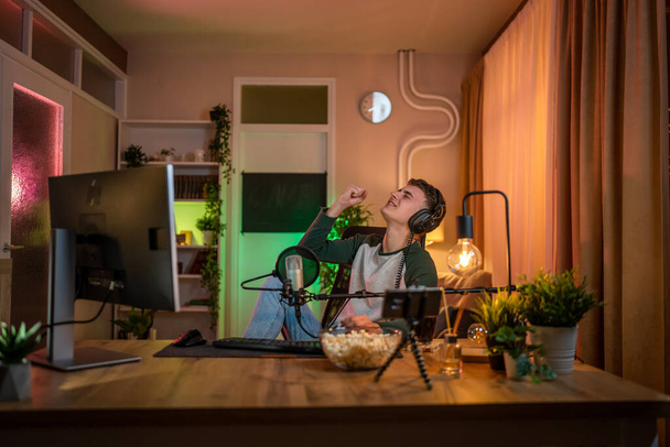 Young man teenager play video games on pc computer while streaming to social media or internet online playtrough walktrough video male gamer having fun at home wear headphone happy winning copy space - Fotografie, Obrázek