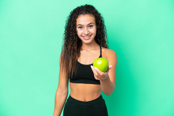 Junge Araberin mit einem Apfel auf grünem Hintergrund mit glücklichem Gesichtsausdruck - Foto, Bild