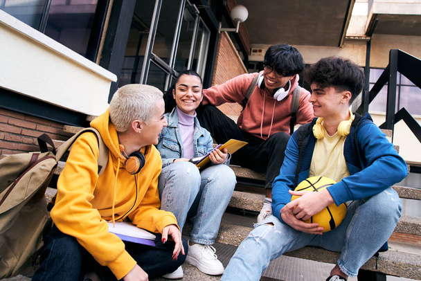 Группа счастливых молодых разнообразных коллег разговаривает и веселится вместе на открытом воздухе в университетском городке. Счастливые подростки разговаривают снаружи здания средней школы. Люди в свободное время. - Фото, изображение