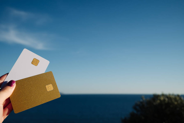 Golden and White Bank Card In Woman Hand On Background Of Scenic View From Arkoudilas Viewpoint, Mountains, Ionian Sea Corfu, Greece. The Concept Of Payment For Relax, Unlimited Possibilities. High - Φωτογραφία, εικόνα
