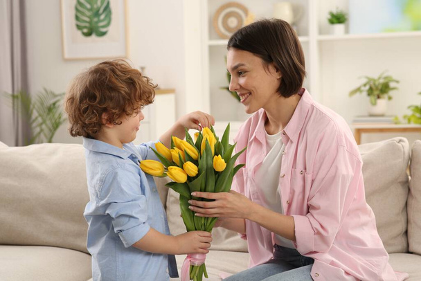Happy woman with her cute son and bouquet of beautiful flowers at home. Mother's day celebration - Fotoğraf, Görsel