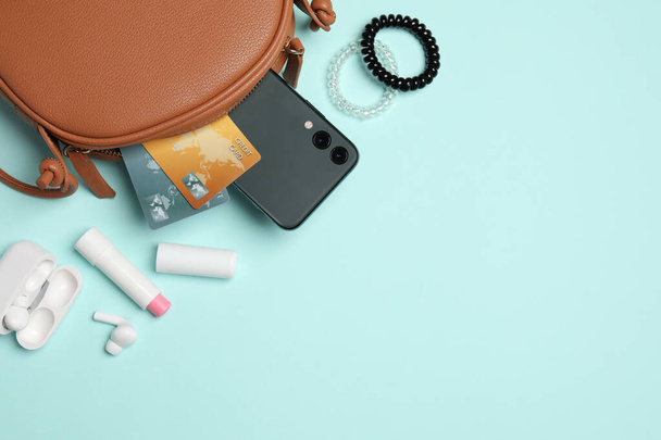 Stylish woman's bag with smartphone and accessories on light blue background, flat lay. Space for text - 写真・画像