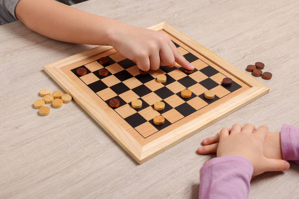 Children playing checkers at light wooden table, closeup - Fotoğraf, Görsel