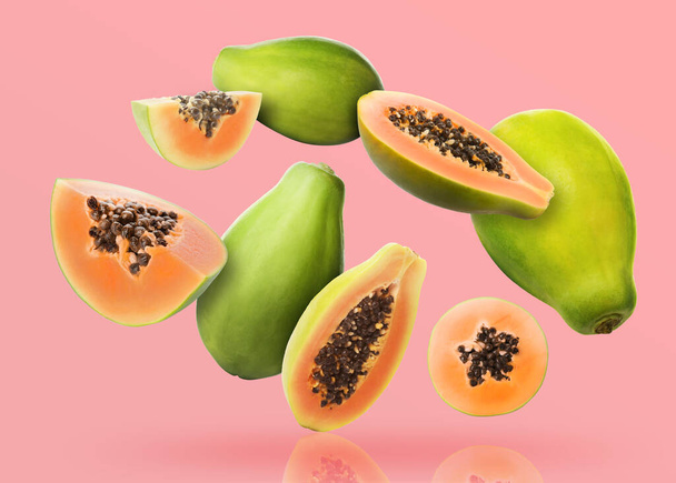 Cut and whole papaya fruits falling on pink background - Photo, Image