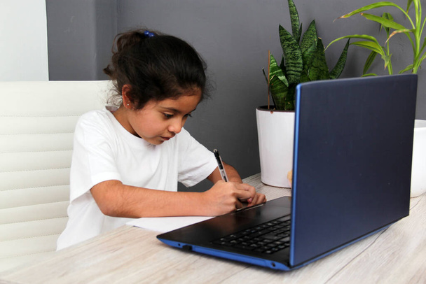 9-year-old Latino girl does home schooling takes online classes at home on a desk with a laptop, studies, is surprised and participates in class - Фото, зображення