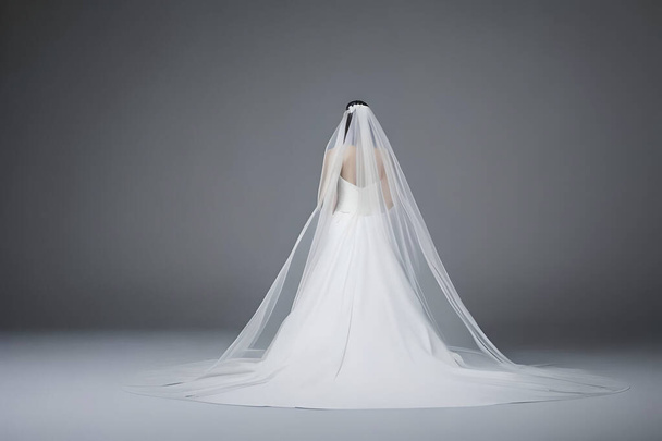 A bride from behind in a white full wedding long dress in a studio, isolated on gray background. - Φωτογραφία, εικόνα