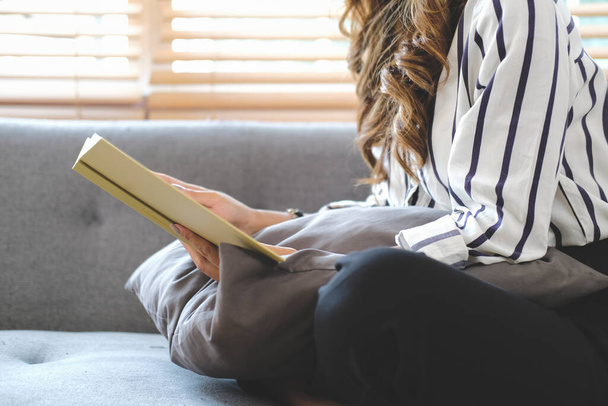 Schnappschuss einer Millennial-Frau, die es sich auf der Couch im hellen Wohnzimmer gemütlich macht und Buch liest. - Foto, Bild