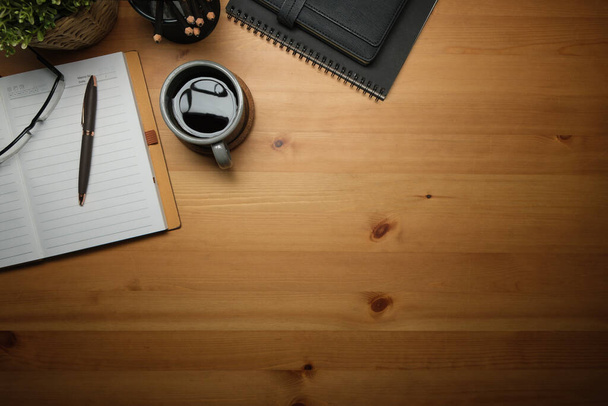 Above view of wooden working desk with cup of coffee, notebook, glasses and alarm clock. Copy space for text. - Fotó, kép