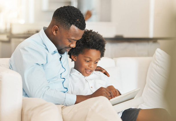 Liebe, Sofa und Vater lesen mit seinem Kind, während sie es sich im Wohnzimmer ihres Hauses gemütlich machen. Glücklicher, verbindender und afrikanischer Mann genießt ein Buch, eine Geschichte oder einen Roman mit seinem Jungen im Haus der Familie - Foto, Bild