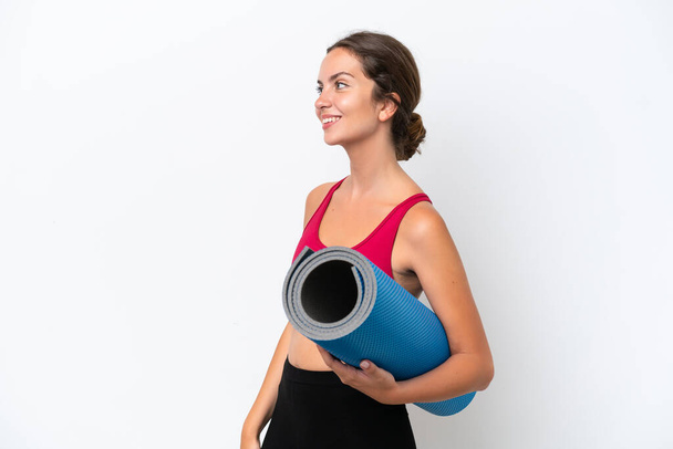 Young sport caucasian woman going to yoga classes while holding a mat isolated on white background laughing in lateral position - Фото, зображення