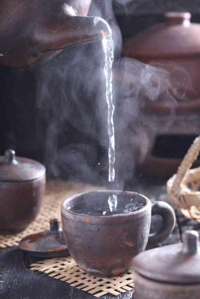 Tea is an aromatic beverage prepared by pouring hot or boiling water over cured or fresh leaves of Camellia sinensis, an evergreen shrub native to East Asia which probably originated in the borderlands of southwestern China and northern Myanmar.  - Foto, afbeelding